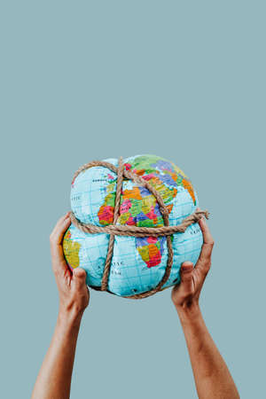 closeup of a man holding an earth globe tightly tied with rope in his hands, on a pale blue backgroundの写真素材