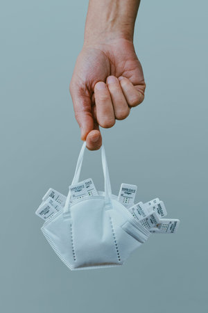 a young man holds a FFP2 face mask full of used covid-19 rapid antigen test devices in his hand, on a gray backgroundの写真素材