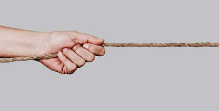 closeup of a caucasian man pulling a rope against a pale gray background, in a panoramic format to use as web banner or headerの写真素材