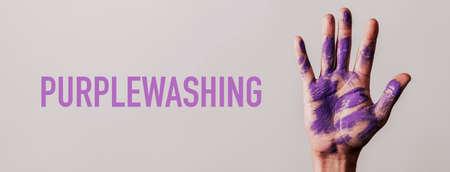 the text purplewashing and the raised hand of a man with stains of purple paint, on a gray background, in a panoramic format to use as web banner or headerの写真素材