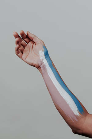 closeup of the arm of a young caucasian person with the transgender pride flag painted in it, on a pale gray backgroundの写真素材