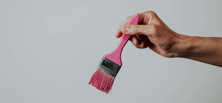 closeup of a man grabbing a paintbrush with some pink paint, on a pale gray background with some blank space on the left, in a panoramic format to use as web bannerの写真素材