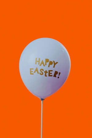 closeup of a blue balloon with the text happy easter written in it, on an orange background with some blank space on topの写真素材