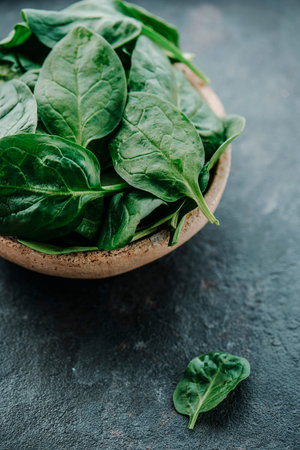 closeup of some fresh spinach leaves in a ceramic bowl, on a dark gray stone surfaceの写真素材