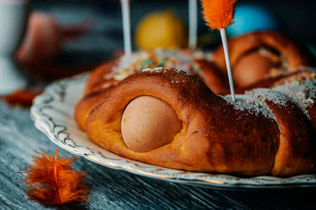closeup of a traditional mona de pascua, a cake eaten in Spain on Easter Monday, ornamented with hard-boiled eggs and feathers of different colors, on a gray wooden tableの写真素材
