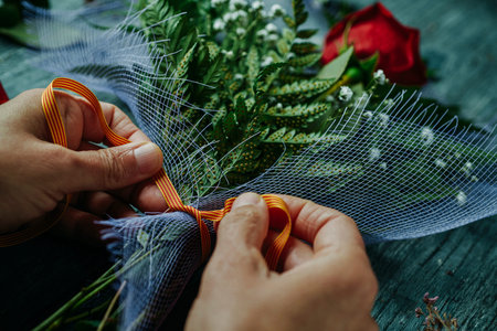 a man ties, with a ribbon patterned with the Catalan flag, a bouquet with a red rose, for Sant...