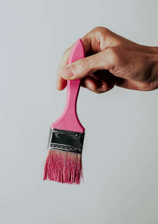 a young man has a paintbrush with some pink paint in his hand, in front of a pale gray backgroundの写真素材