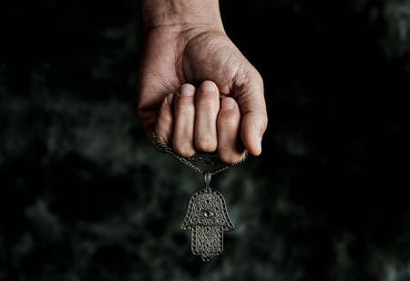 a man is holding an old hamsa amulet, also known of the hand of fatima or the hand of mary, on a black mottled backgroundの写真素材