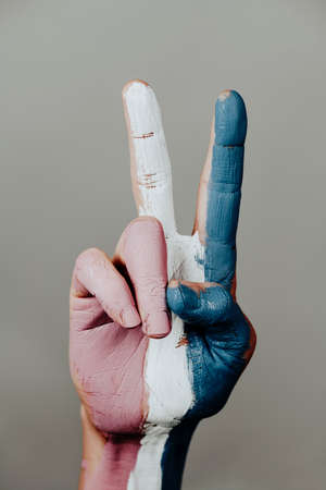 the hand of a person doing the V-sign with the transgender pride flag painted in it, on a pale gray backgroundの写真素材