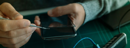 closeup of a man removing the broken screen protector of a smartphone, sitting at a table or...