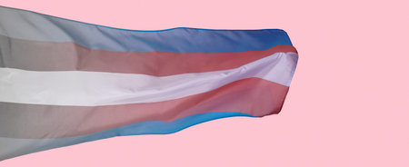 closeup of a gradient transgender pride flag waving in the air on a pink background, in a panoramic...