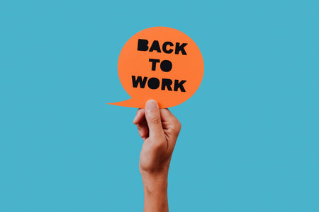 man holds an orange paper sign, in the shape of a speech bubble, with the text back to work in it,...