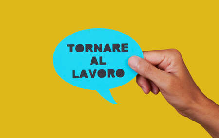 closeup of a man holding a blue paper speech bubble with the text back to work written in italian, on a yellow backgroundの写真素材
