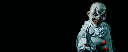 a creepy evil clown, in a gray costume with a white ruff around his neck, against a black background with some blank space on the left, in a panoramic format to use as web banner or headerの写真素材