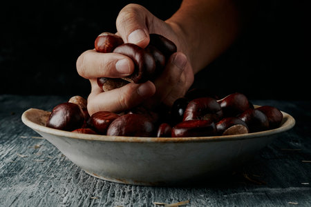 closeup of a young man taking a handful of chestnuts from an old and weathered white ceramic plate, placed on a rustic gray wooden tableの写真素材