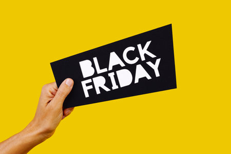closeup of a man hacving a black sign in his hand with the text black friday, on a yellow backgroundの写真素材