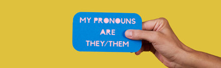 a person holds an blue paper sign with the text my pronouns are they, them on a yellow background, in a panoramic format to use as web banner or headerの写真素材