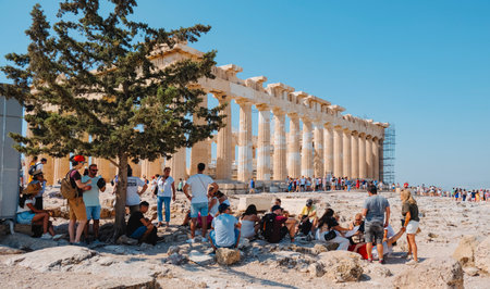Athens, Greece - August 30, 2022: Visitors protecting themselves from the intense sun of a summer day in the shade of a tree, in front of the famous Parthenon, in the Acropolis of Athens, Greeceのeditorial素材