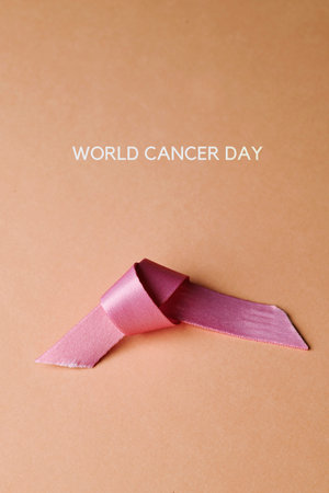the text world cancer day and a used pink awareness ribbon on a pale pink background