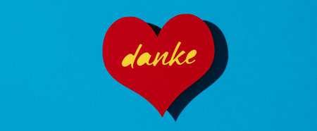 a red heart-shaped sign reads thank you in german on a blue background, in a panoramic format to use...