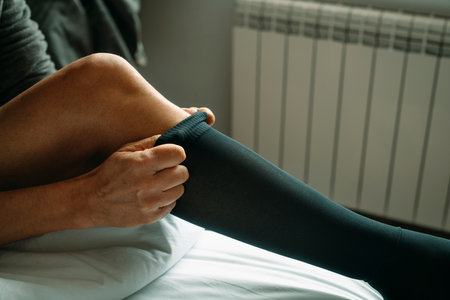 closeup of a man putting on a compression sock sitting on the bed at homeの写真素材