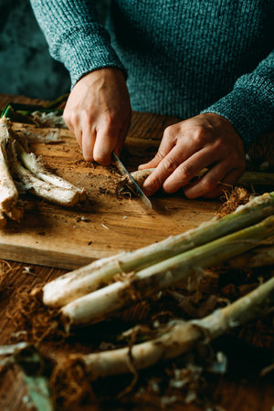 closeup of a man cutting the roots of some raw calcots, sweet onions typical of Catalonia, Spain, with a kitchen knife, on a wooden cutting boardの写真素材
