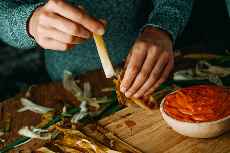 closeup of a man peeling a roasted calcot, a sweet onion typical of Catalonia, Spain, before to dip...