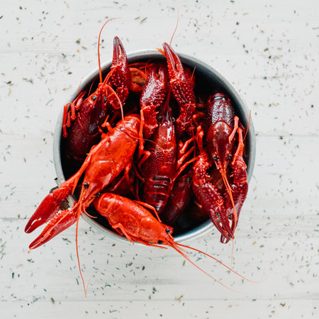 high angle view of some cooked crayfishes in an old metal container, on a white surface sprinkled with different culinary herbsの写真素材