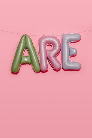 some alphabet-shaped balloons of different colors forming the text are hanging from a string on a pink backgroundの写真素材