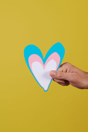 closeup of the hand of a young caucasian person holding a heart with the colors of the transgender...