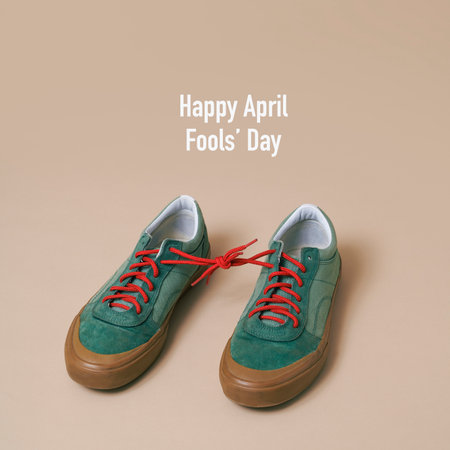 the text happy april fools day and a pair of green sneakers with its shoelaces tied together, on a pale brown backgroundの写真素材