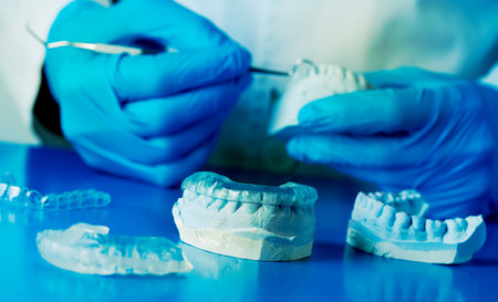 closeup of a dentist, wearing blue latex gloves, adjusting an occlusal splint, using a mouth cast