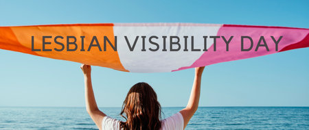 the text lesbian visibility day and a woman holding a lesbian pride flag above her head on the sky, in a panoramic format to use as web bannerの写真素材