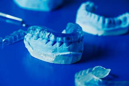 closeup of a occlusal splint in a dental mold on a blue surface next to some other dental molds and occlusal splintsの写真素材