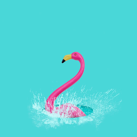 closeup of a fake pink flamingo splashing in a puddle of water, on a blue backgroundの写真素材