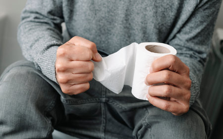 a caucasian man, sitting in the toilet, grabs tight the toilet paperの写真素材