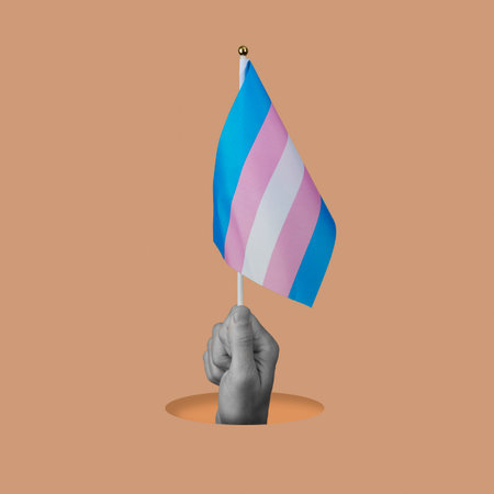the hand of a person in black and white waving a transgender pride flag peeping out of a hole on a orangish pink backgroundの写真素材