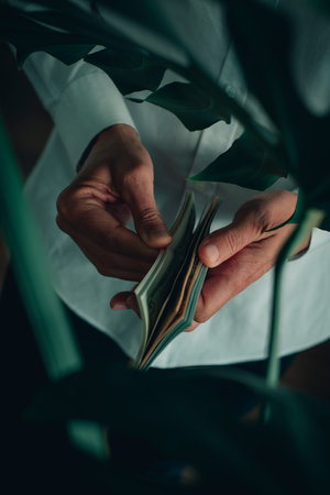 a man, wearing a white long-sleeve shirt, counts some dollar notes, indoors, as seen through the...