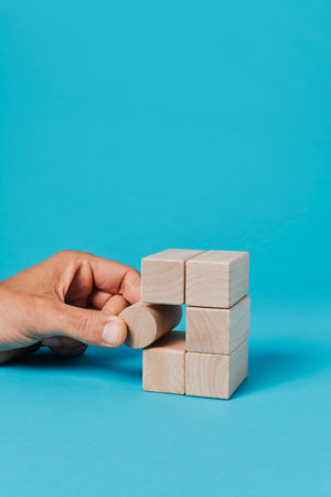 a man puts a cylindrical toy block in a stack of rectangular toy blocks, on a blue background with...