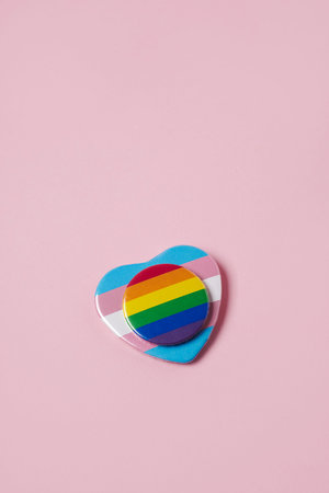 a round badge patterned with a rainbow flag on a heart-shaped badge patterned with a transgender...