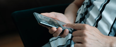man, sitting on sofa, gives a like to the profile of another man in a simulated online dating app on his smartphone, in a panoramic format to use as web banner or headerの写真素材