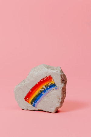 closeup of a rock with a rainbow flag painted on it, on a pink background with some blank space on topの写真素材