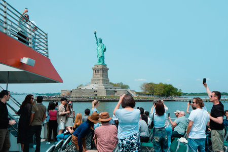 New York City, United States - May 22, 2023: A tour boat browsing in front of the Statue of Liberty, in Liberty Island, New York, United States, on a sunny spring dayのeditorial素材