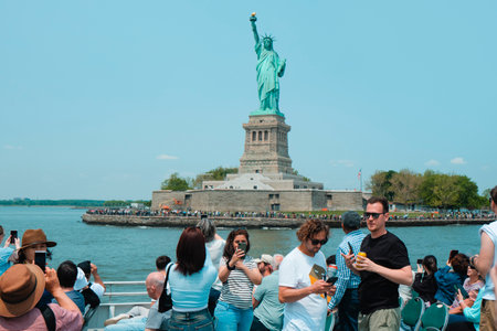 New York City, United States - May 22, 2023: A tour boat full of tourists browses in front of the Statue of Liberty, in Liberty Island, New York, United States, on a sunny spring dayのeditorial素材