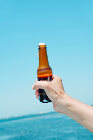 closeup of a man with a beer bottle in his hand in front of the waterの写真素材