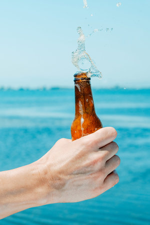 closeup of a man splashing some beer from a bottle in front of the waterの写真素材