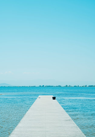 a weathered wooden pier leading to the water, with a pair of black flip-flops and a black bucket in...