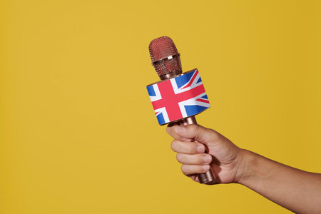 a man has a microphone patterned with the union jack, the flag of the united kingdom, in his hand, on a yellow backgroundの写真素材