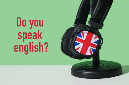 the question do you speak english and a pair of headphones patterned with the flag of the united kingdom, on a white surface, in front of a green backgroundの写真素材