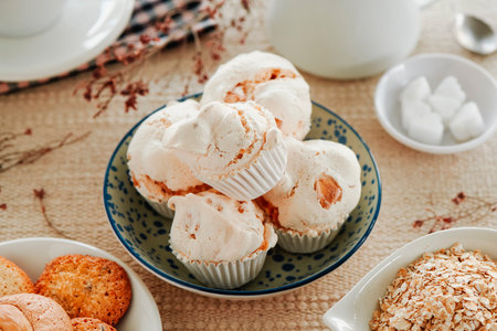 closeup of some merengues almendrados, spanish baked meringues with almonds, in a white ceramic bowl on a table set with a brown tablecloth next to a plate with cookiesの写真素材